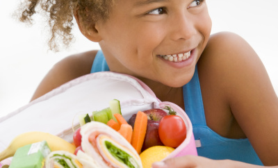 Young girl holding packed lunch in living room smiling